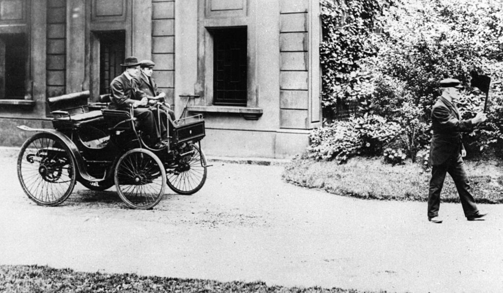 C.S. Rolls am Steuer seines Peugeot von 1896. Vorneweg geht ein Fußgänger mit Warnflagge (gemäß Locomotive Act 1865)