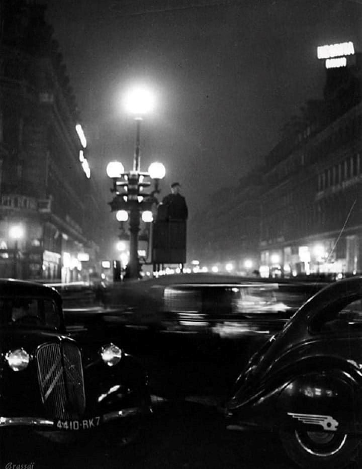 Das Kennzeichen läßt auf die 30er Jahre schliessen, die Beleuchtung und das Verkehrsaufkommen auf die Pariser Innenstadt. Rechts ein Peugeot 402.