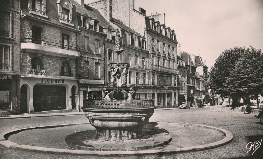 Diese Karte ist 1954 gelaufen. Sie zeigt den Place du Centre mit der Fontaine de la Pompe und im Hintergrund einen Peugeot 202