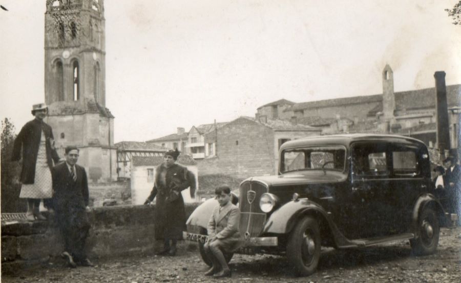 Eindeutig 1930er. Vor dem Hintergrund von Kirche und Glockenturm posiert eine Familie vor ihrem Peugeot 201 für den Fotografen